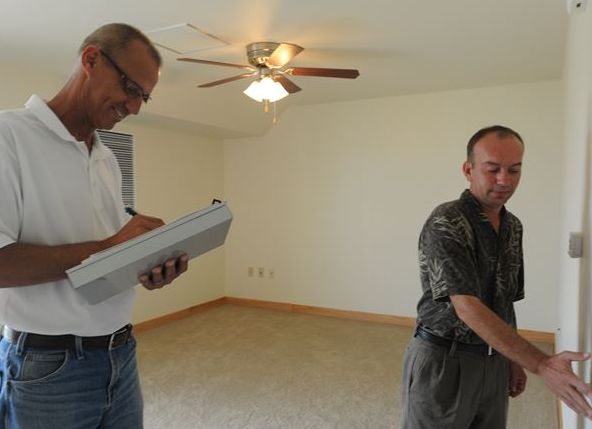A man with clipboard signing off as another man inspects an apartment