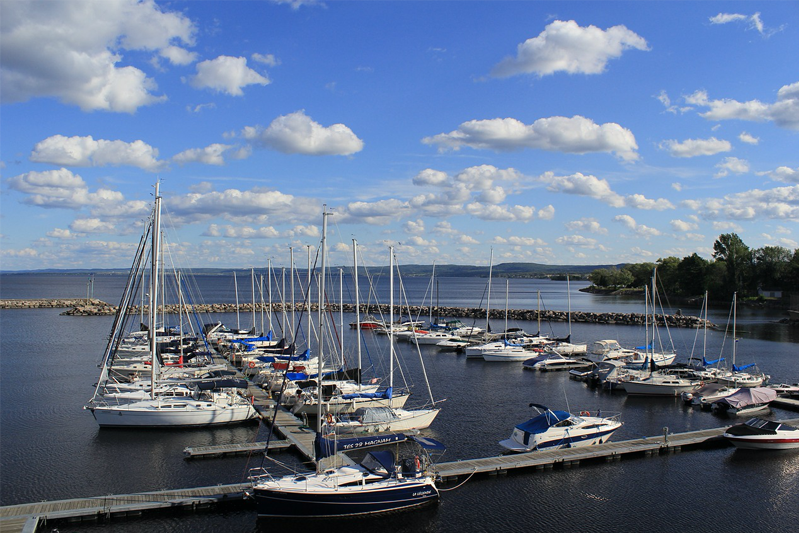 Sailboats and motorboats moored on both sides of two piers coming off another pier with a breakwater behind them in a quiet marina.