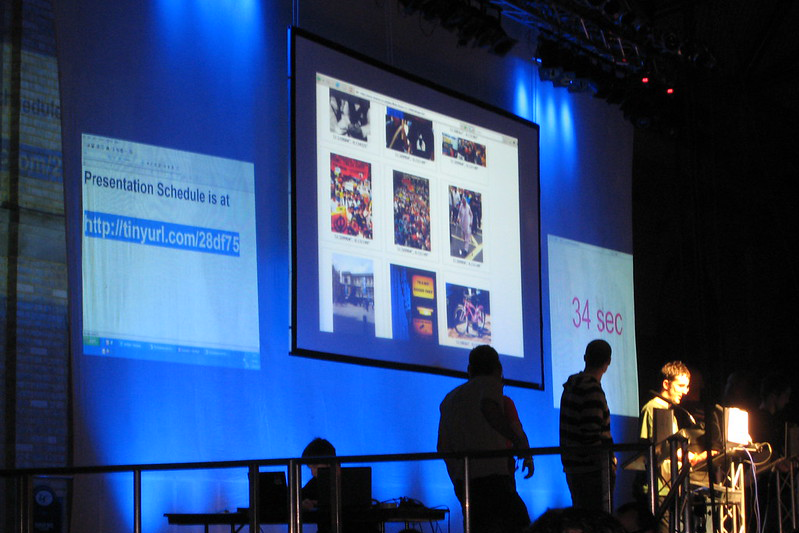 Three presentations are displayed on a huge screen behind the speaker