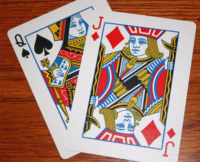 A queen of spades and a jack of diamonds on a wood background