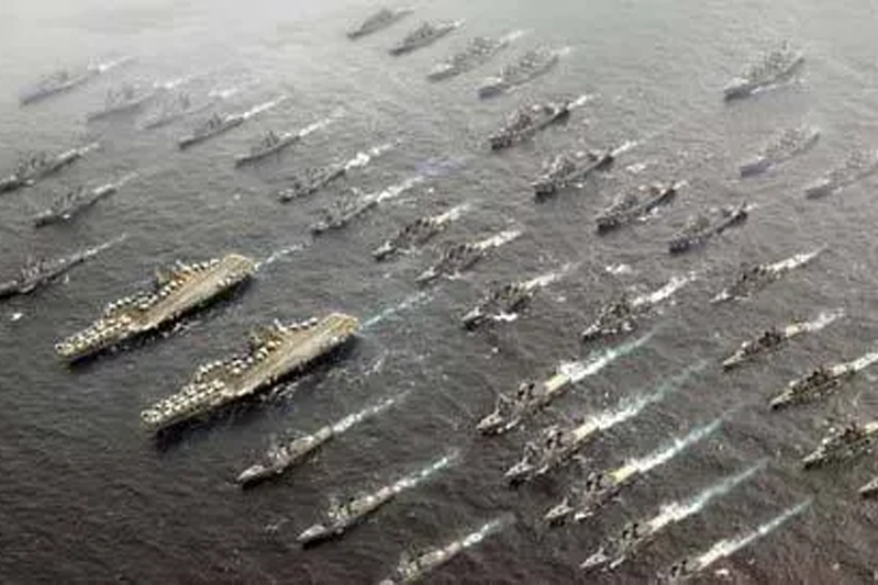 Overhead look of a fleet of ships steaming forward in a black-and-white photo