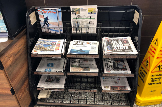 Different newspapers in stacks on a rack.