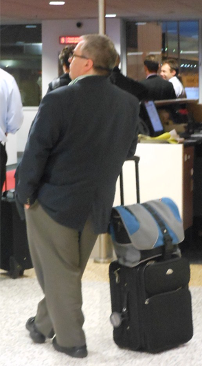 The back of a man in a suit casually leaning against his luggage.