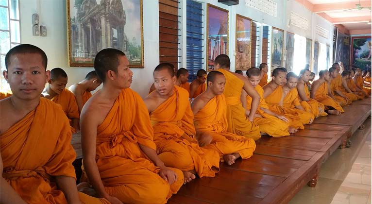 Novice Theravada monks robed in orange prepare for morning chanting.