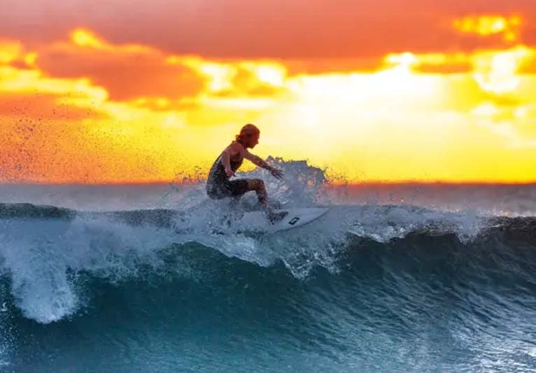 A woman surfing a wave with a sunset in the background.