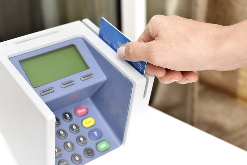 A female hand sliding a debit or credit card through a blue point-of-sale machine. She could be making a retail purchase,