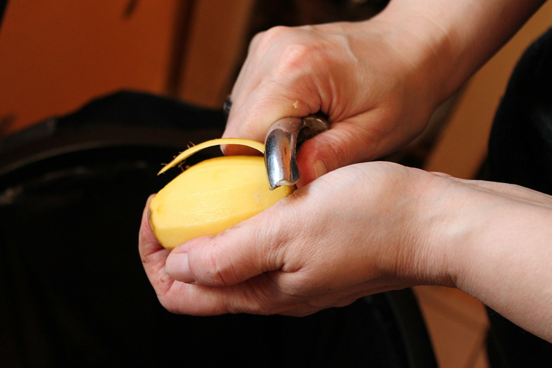 Close-up of hands peeling a potato with a potato peeler