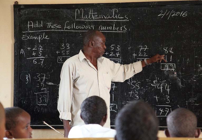 A blackboard filled with mathematical problems with a teacher pointing them out to his students.