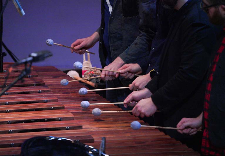 Close-up of three people playing a xylophone.