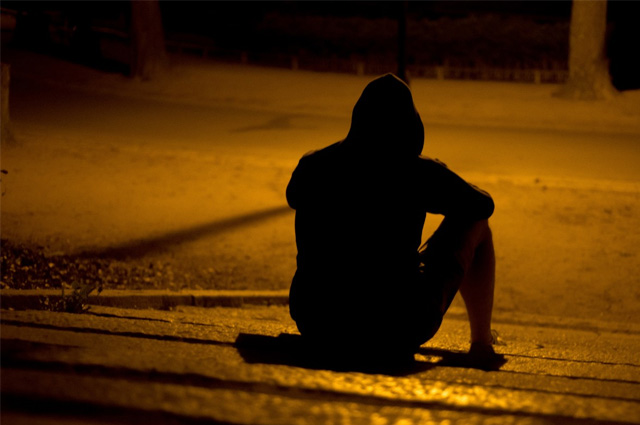 Silhouette of a person wearing a hoodie and sitting on stairs under the orange glow of a street light