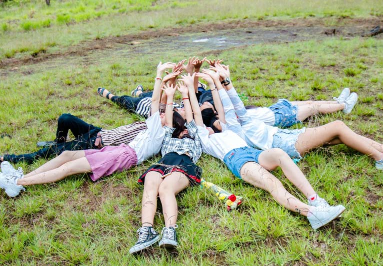 Group of friends form a circle while lying on the grass with their hands on top.