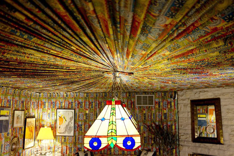 A vibrant printed fabric in red, yellow, and green is pleated and radiates out from a central point on a ceiling.