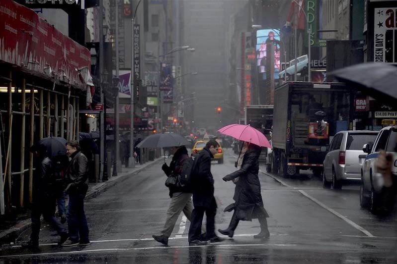 Pedestrians with umbrellas walking across a cross walk in the rain.