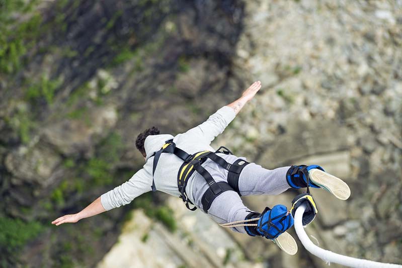 A close-up of a man in sweats jumping from a cliff.
