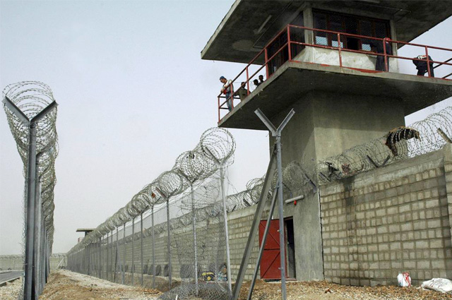 Exterior boundary with a guard tower and two rows of fencing topped with razor wire.