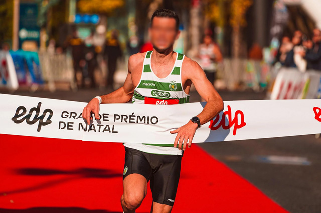 A dark-haired an in a green-and-white striped tank and black bike shorts running on a red carpet into a wide white banner with the race's name on it.