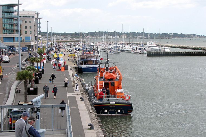 Several boats, including the  orange Severn class lifeboat, are pulled alongside the concrete quay.