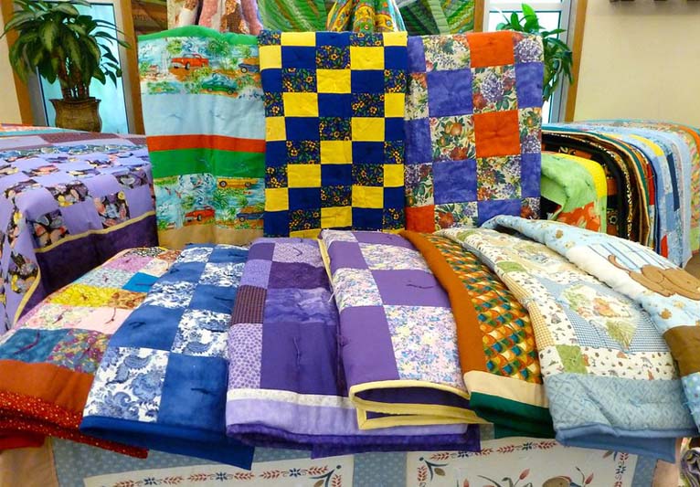 A range of quilts displayed on a rack and folded on a table.