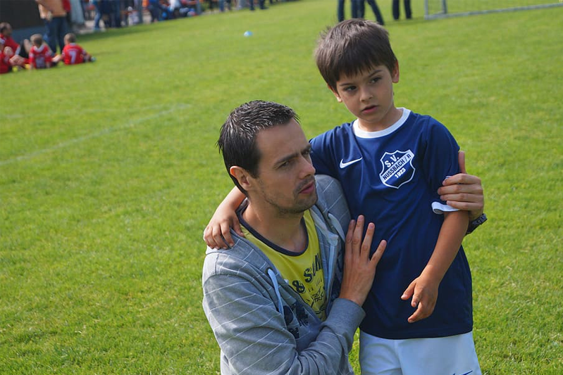 Father kneels by son in soccer uniform, consoling his disappointment