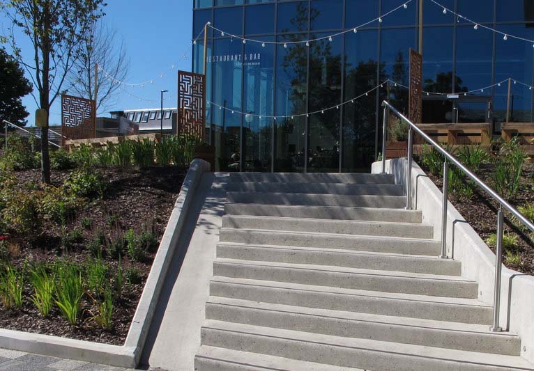 A narrow concrete channel rides beside a concrete staircase coming from a building.