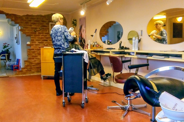 A beautician stands behind a tall blue cart as they work on someone's hair.