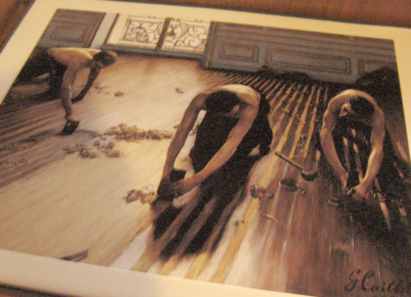 3 men on their knees scraping varnish off a wood floor