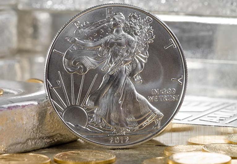 A silver American Eagle coin standing on end amid other coins