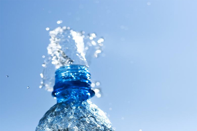 Close-up of the opening of a bottle with water splattering up.