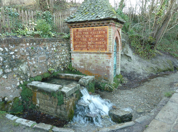 A brick-built open-top box allows the water to flow out of the bank. It's in front of a small brick-built shrine-like building.