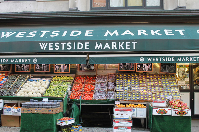 A frull frontal of outdoor bins of vegetables under a green awning.