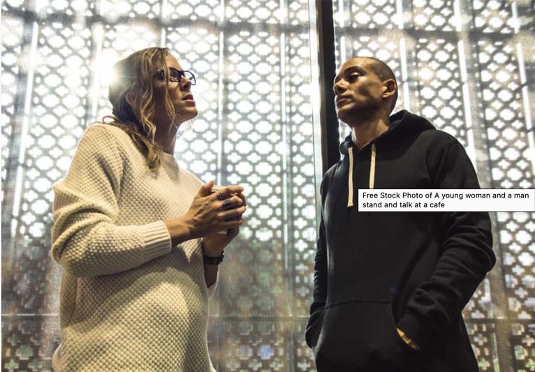 A blonde woman in a cream sweater is talking to a short-haired man in a dark hoodie.
