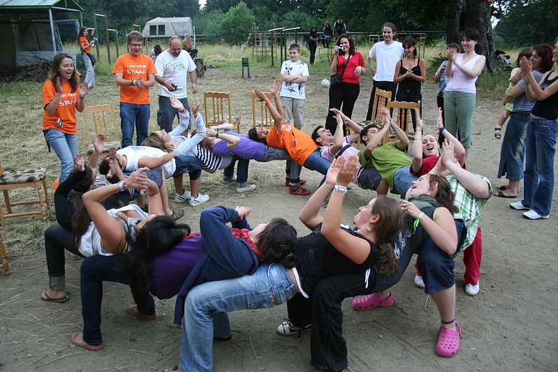 A ring of people bent at the knee with their chests resting on the person's knees behind them.