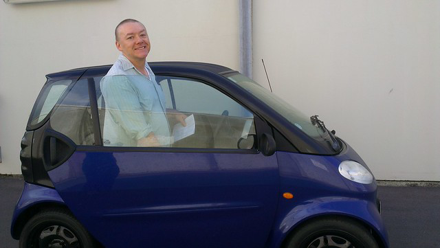 Man getting into the deep royal blue Smart Fortwo, tiny car