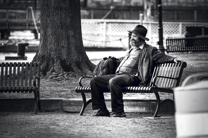 Black-and-white photo of a bearded man, sitting exhausted on a park bench