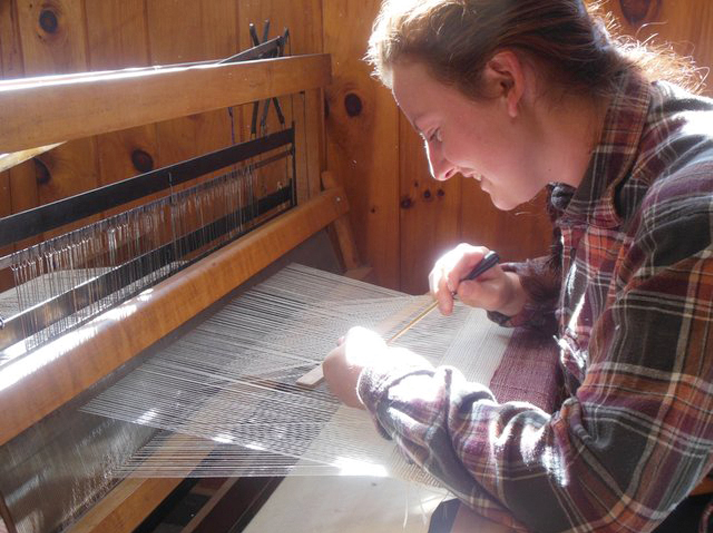 Woman leaning over a loom, weaving.