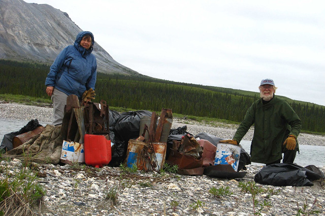 Park staff and volunteer next to a pile of trash gathered from cleaning up old backcountry campsite debris, getting it ready to be flown out.