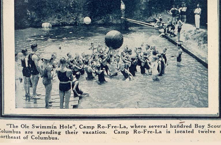 A grainy black-and-white photograph of boys in old-fashioned bathing suits playing in a pool.